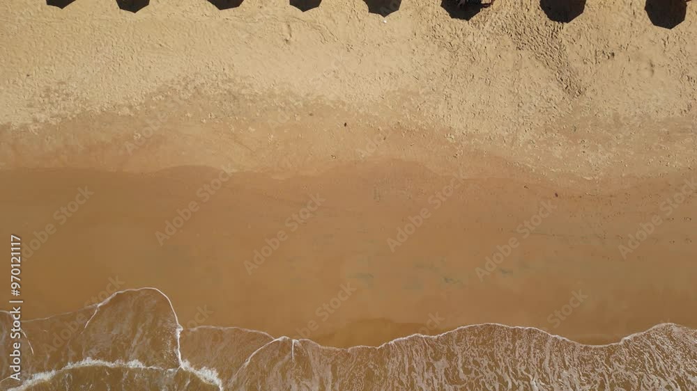 Imagem aérea da praia de Castelhanos em Anchieta, em uma manhã ensolarada. Praia deserta, ondas do mar e barracas na areia.