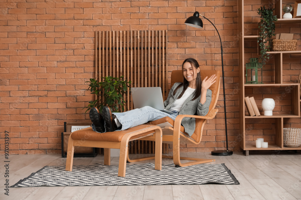 Fototapeta premium Young woman sitting in armchair and using laptop at home