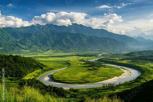 A winding river flows through a lush valley, surrounded by towering green mountains and a clear blue sky.