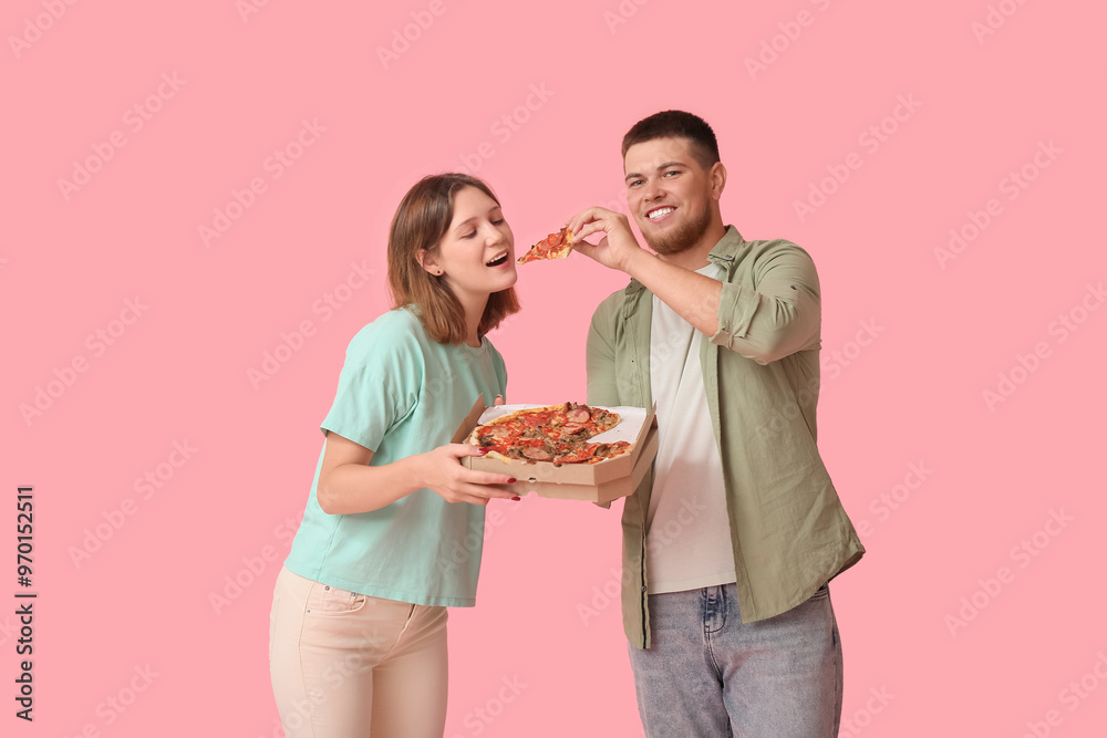 Beautiful young happy couple with cardboard box of tasty pizza on pink background Beautiful young happy couple with cardboard box of tasty pizza on pink background