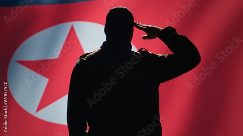 Conscript doing saluting hand gesture towards North Korea flag in command center, showing respect. Military unit in uniform serving in Korean Peoples Army, doing honoring gesturing, camera A photo