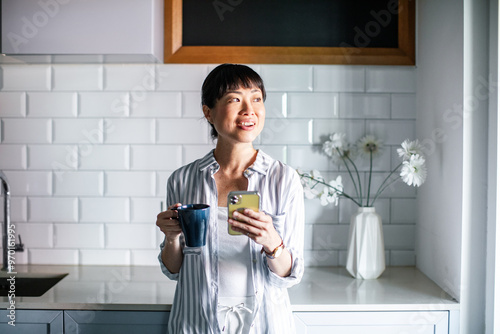 Asian woman using smartphone in the home kitchen photo