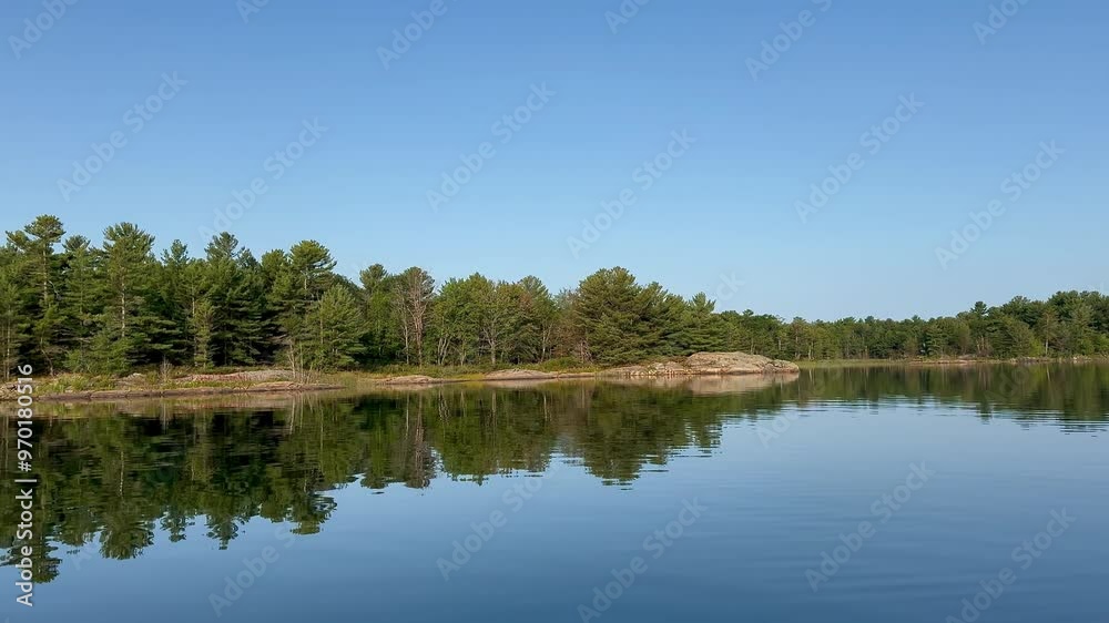 Evergreen forest and rocky shore reflected in a calm lake Evergreen forest and rocky shore reflected in a calm lake
