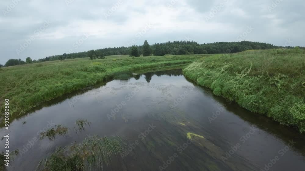Flying an FPV drone over serene river reflecting the cloudy sky runs through a lush, green landscape. Flying an FPV drone over serene river reflecting the cloudy sky runs through a lush, green landscape.