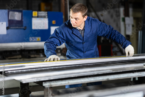 Portrait of worker with tape measure who measures sheet of iron using tape measure and marks the cutting line