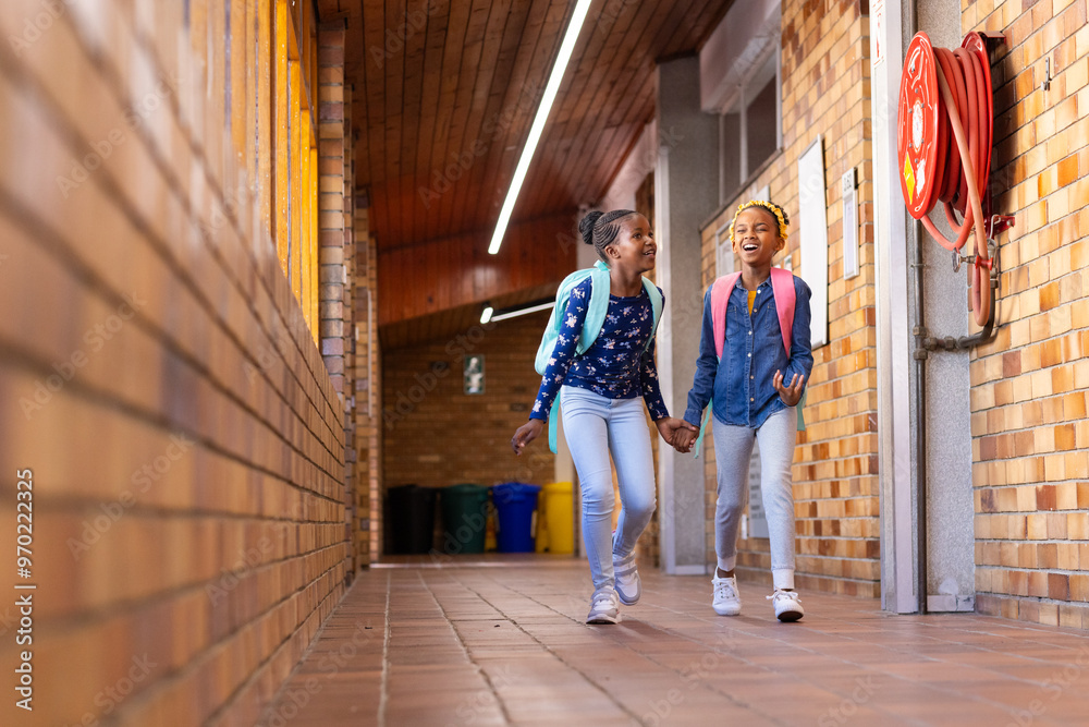 Walking in school hallway, two african american girls with backpacks smiling and holding hands Walking in school hallway, two african american girls with backpacks smiling and holding hands