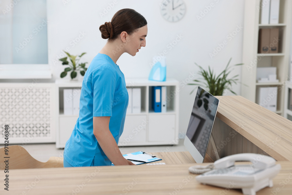 Professional receptionist working at wooden desk in hospital Professional receptionist working at wooden desk in hospital