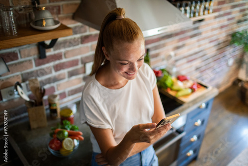 Smiling young woman using smartphone in modern kitchen