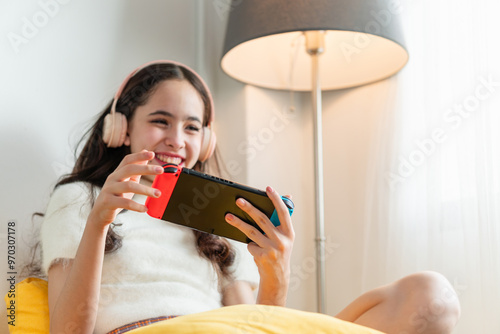 Cheerful young girl play game in living room, Teenage girl in headphones having fun playing with portable gaming console photo