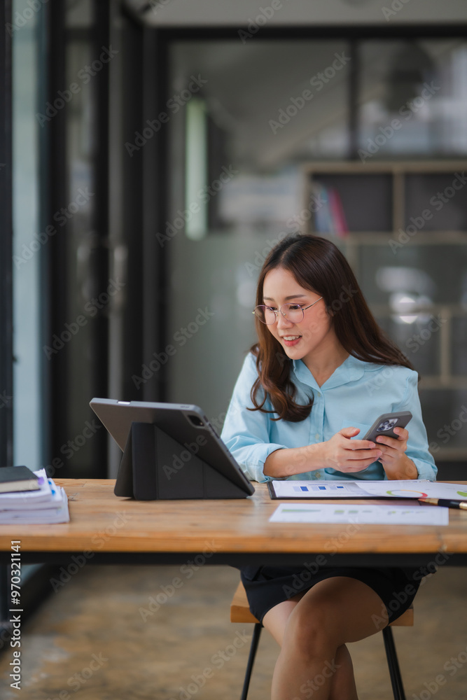 Focused and Connected: A young businesswoman sits at her desk, effortlessly multitasking between her tablet and smartphone, showcasing her dedication and efficiency in a modern and stylish office sett Focused and Connected: A young businesswoman sits at her desk, effortlessly multitasking between her tablet and smartphone, showcasing her dedication and efficiency in a modern and stylish office sett