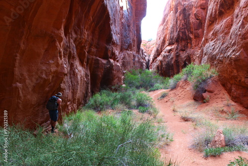 Man walks through passage in between red rocks 