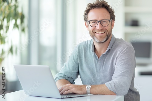 Smiling man working on a laptop in a bright, modern office environment