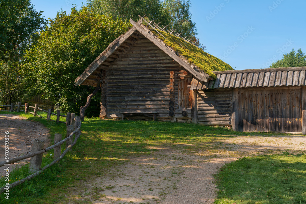 View of an ancient log outbuilding on the territory of the Pushkin village in Bugrovo of the Pushkin Museum-Reserve on a sunny summer day, Pushkinskiye Gory, Pskov region, Russia View of an ancient log outbuilding on the territory of the Pushkin village in Bugrovo of the Pushkin Museum-Reserve on a sunny summer day, Pushkinskiye Gory, Pskov region, Russia