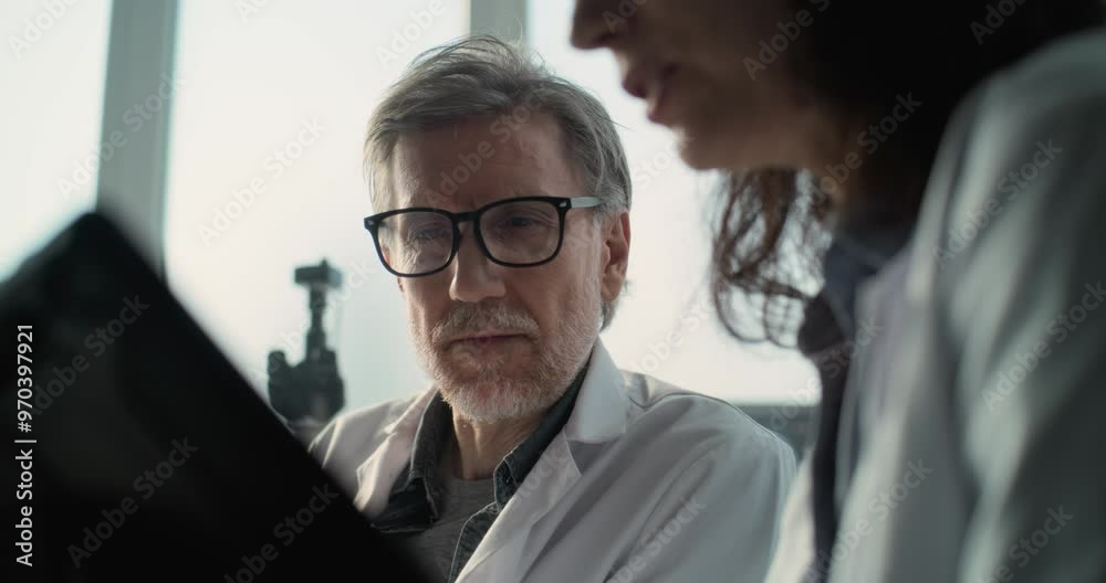 Close up of male and female scientists in lab coats conducting scientific research, looking at tablet computer and having discussion. Archaeologists work in modern archaeological science laboratory. Close up of male and female scientists in lab coats conducting scientific research, looking at tablet computer and having discussion. Archaeologists work in modern archaeological science laboratory.
