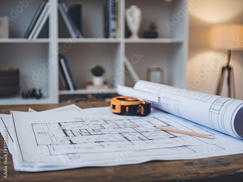 Blueprints spread out on a wooden table with a measuring tape and pencil photo