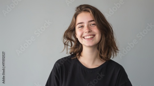 A young woman is smiling while standing in front of a plain gray background. Her expression is cheerful and relaxed as she looks directly at the camera, panorama with copy space