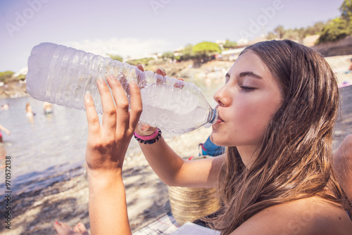 Young girl at the beach drinking water out of a plastic bottle. photo