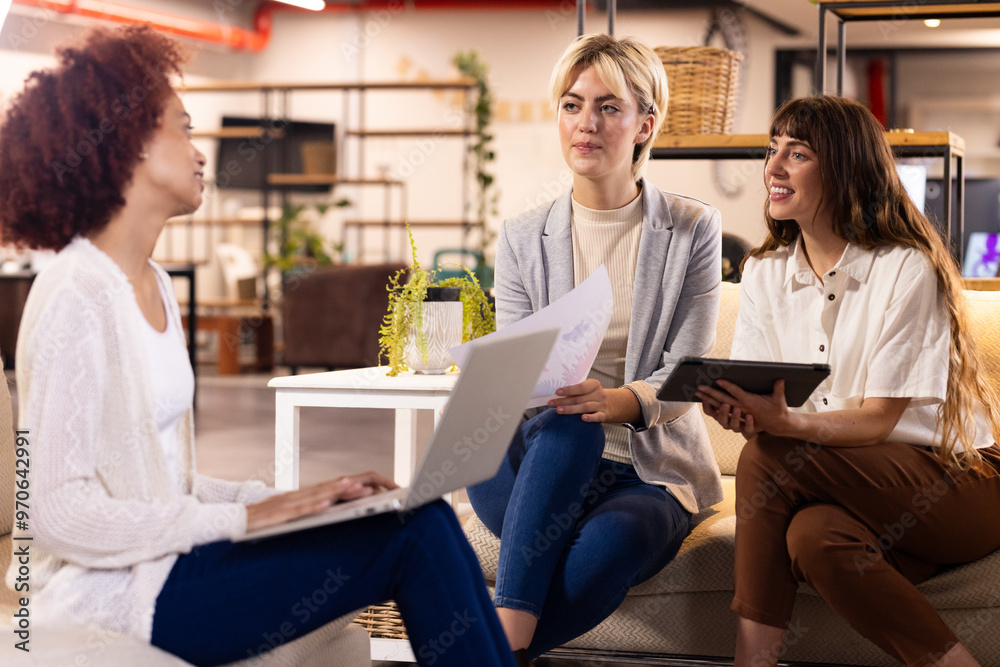 At office, discussing creative writing business, three multiracial women using laptop and tablet At office, discussing creative writing business, three multiracial women using laptop and tablet