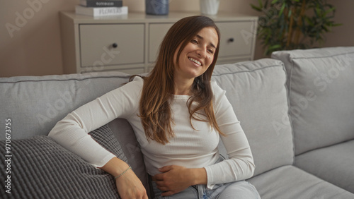 A young woman relaxing on a couch in her living room, smiling comfortably in a casual home interior environment, surrounded by simple modern decor. Free Download A young woman relaxing on a couch in her living room, smiling comfortably in a casual home interior environment, surrounded by simple modern decor. - GFXLoad