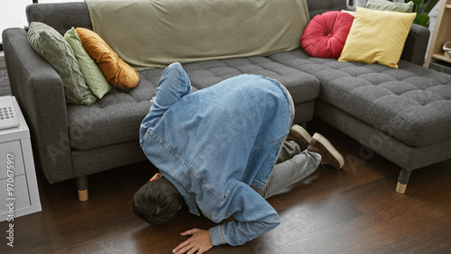 Εκτύπωση καμβά Young man in denim searching under couch in modern living room interior