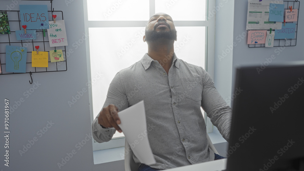 Handsome young man in an office holding a paper and looking up with a beard and bald head against a bright window