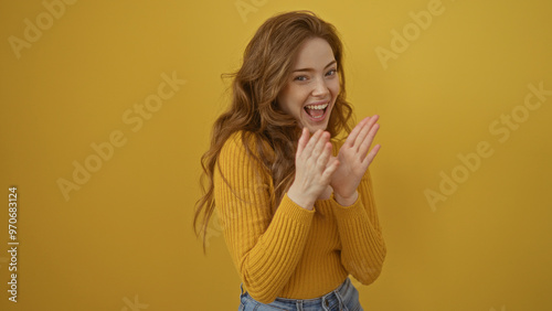 A young blonde woman is clapping and smiling joyfully against an isolated yellow background wall. photo