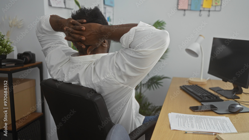 A young african american man relaxes at a desk in an office, hands ...