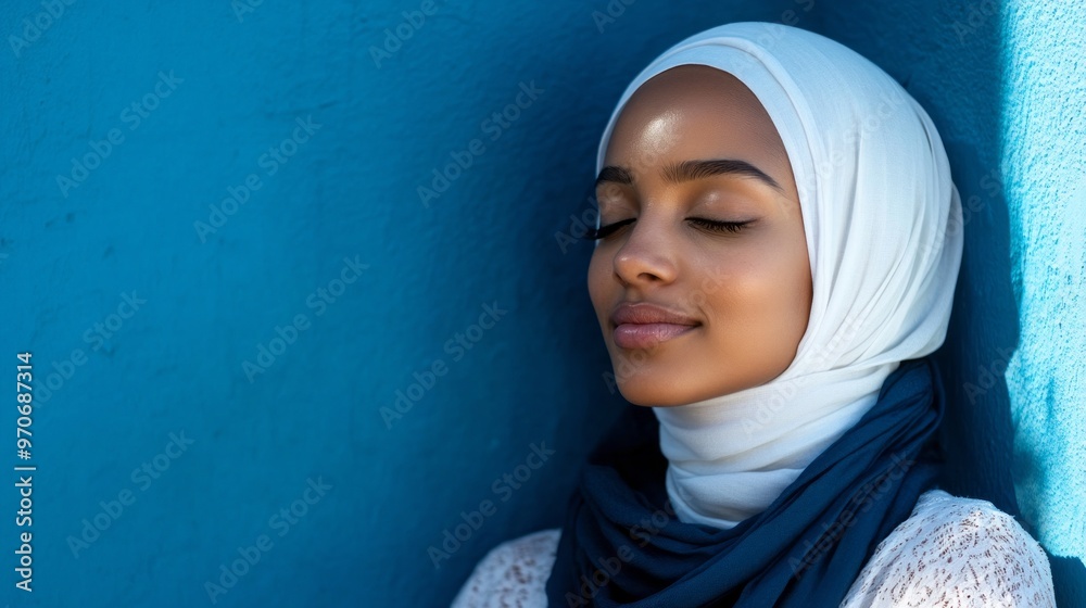 A young woman wearing a white hijab leans her head against a bright blue wall, eyes closed, savoring a peaceful moment in an urban environment filled with color A young woman wearing a white hijab leans her head against a bright blue wall, eyes closed, savoring a peaceful moment in an urban environment filled with color