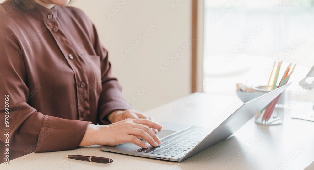 A woman is typing on a laptop computer. She is wearing a brown shirt and has a pen on the table in front of her. suggests a work or study environment, where the woman is focused on her task
