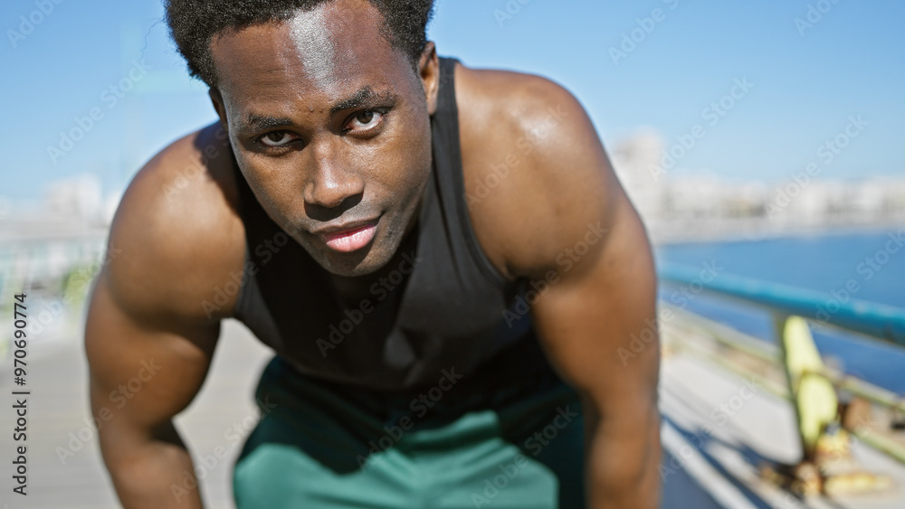 Young african american man in workout gear resting near the seaside with a blurred beach backdrop. Young african american man in workout gear resting near the seaside with a blurred beach backdrop.