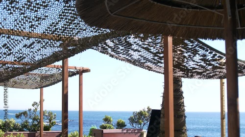 Empty beach restaurant and bar with palm trees and umbrellas in summer,  next to the ocean. Pan down from the sky to the sea.