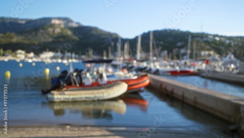 Blurred image of boats docked at a marina with mountains in the background, emphasizing a peaceful harbor setting with soft focus.