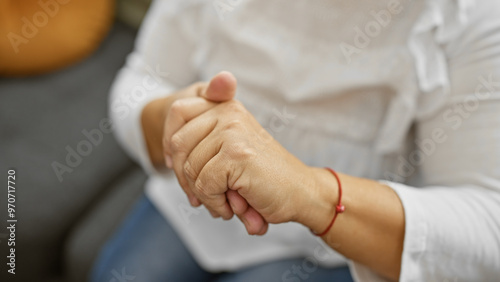 A close-up of a mature woman's hands clasped together indoors, suggesting contemplation or rest. photo