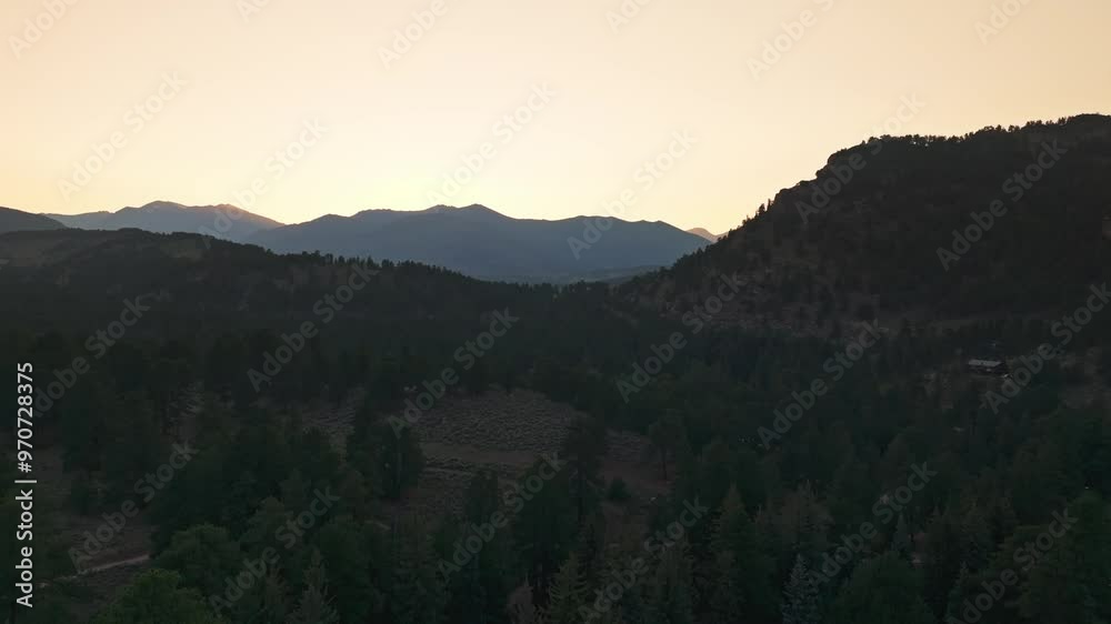 Drone view of forested mountains during sunset, with warm light fading behind the distant ridges Drone view of forested mountains during sunset, with warm light fading behind the distant ridges