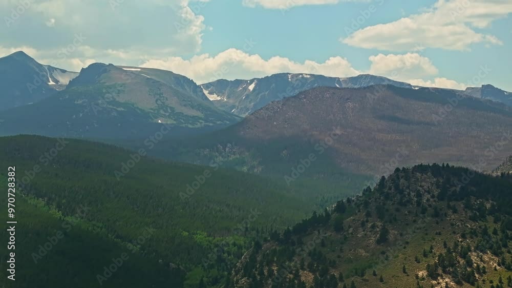 Aerial shot of vast mountain range and forested valleys with distant peaks under a partly cloudy sky Aerial shot of vast mountain range and forested valleys with distant peaks under a partly cloudy sky