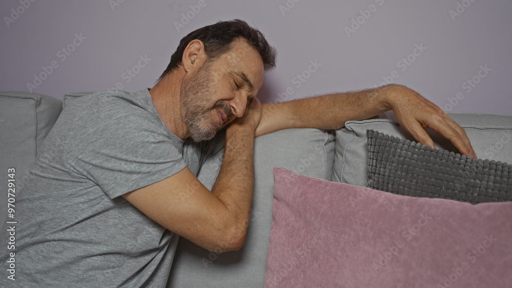 Obraz premium Middle-aged hispanic man sleeping in a living room with grey and pink pillows in a cozy home interior environment