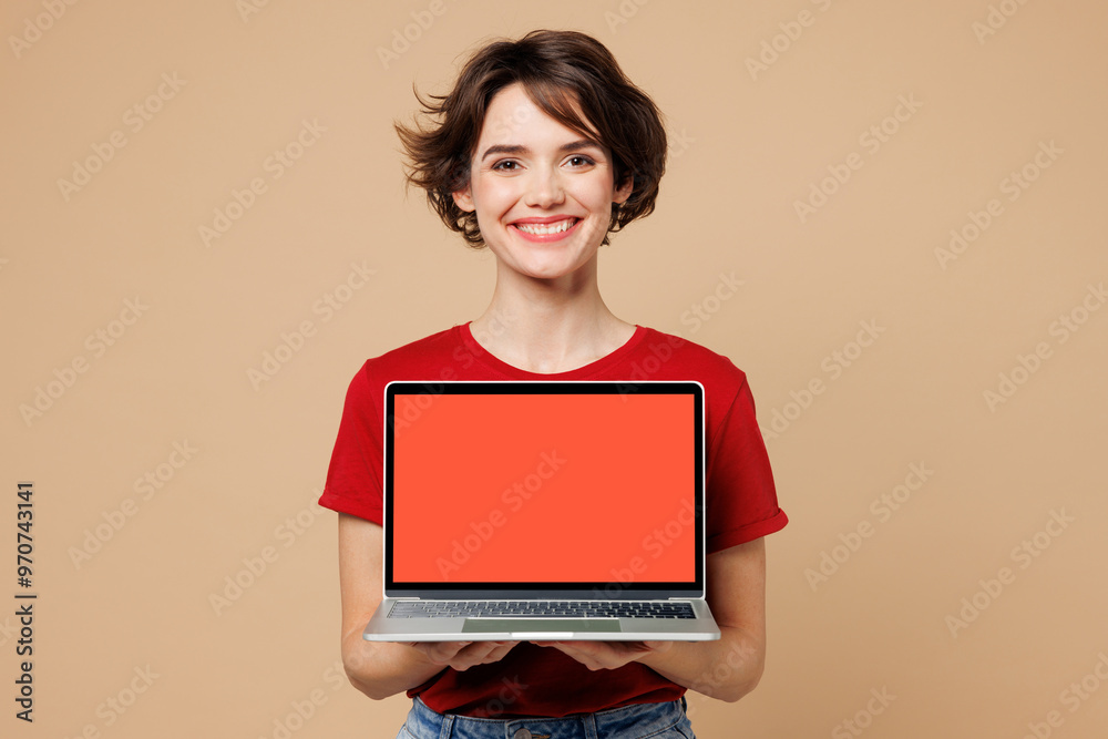 Young smiling happy IT woman she wears red t-shirt casual clothes hold use work on blank screen laptop pc computer isolated on plain pastel light beige background studio portrait. Lifestyle concept. Young smiling happy IT woman she wears red t-shirt casual clothes hold use work on blank screen laptop pc computer isolated on plain pastel light beige background studio portrait. Lifestyle concept.