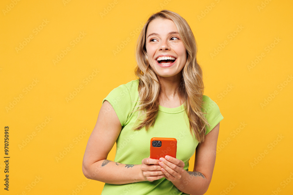 Φωτογραφία Young happy smiling blonde woman wears green t-shirt casual clothes hold in hand use mobile cell phone look aside on area mockup isolated on plain yellow orange background studio