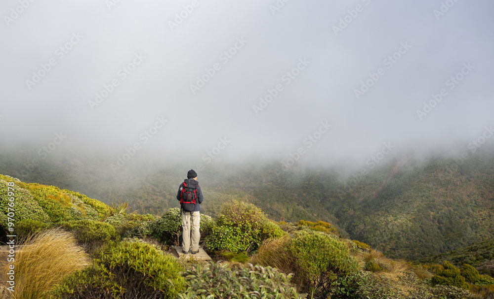 Backpacker enjoying the views of mountains in the clouds. Pouakai circuit. Egmont National park. New Zealand.