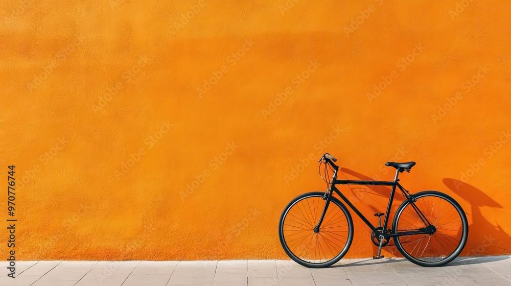 Naklejka premium A modern bicycle parked against a bright orange wall, emphasizing urban living and modern design.