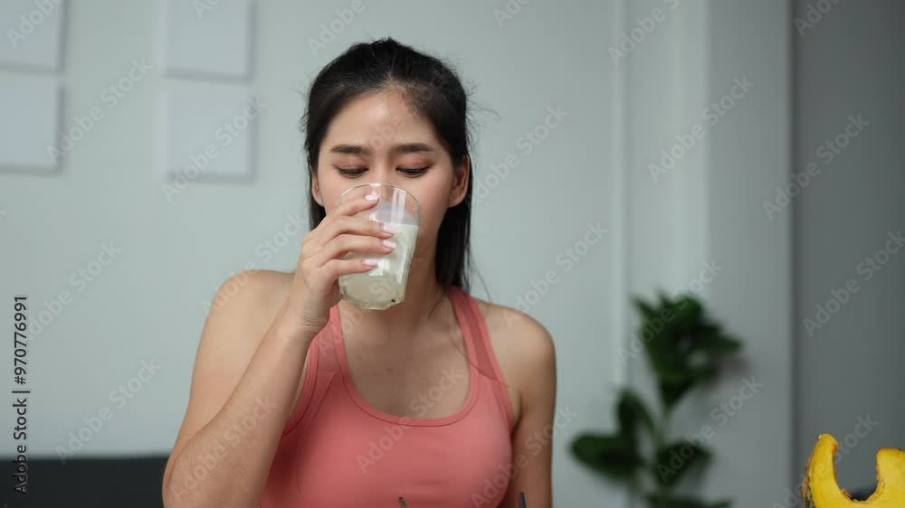 Happy beautiful Asian woman sitting holding a glass of milk after exercise. Fitness at home Healthy woman smiles and drinks protein milk. Vegetable salad. Health and weight loss concept.