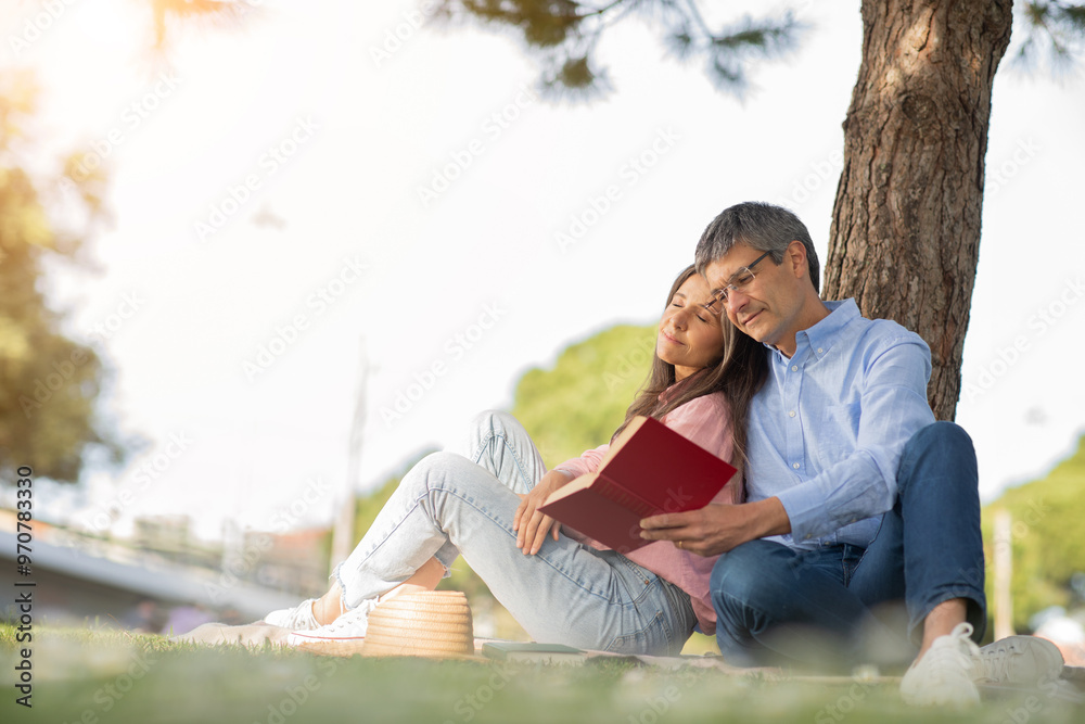 A couple enjoys a cozy moment under a tree, sharing a book in a sunny park. Their relaxed posture and warm expressions reflect a peaceful spring afternoon together. A couple enjoys a cozy moment under a tree, sharing a book in a sunny park. Their relaxed posture and warm expressions reflect a peaceful spring afternoon together.