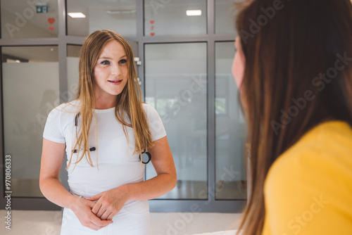 A healthcare professional in a white outfit with a stethoscope engages in conversation with a patient. The setting is modern and bright, suggesting a medical office or clinic.