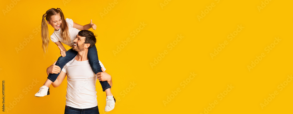 Obraz premium A father carries his daughter on his shoulders, both smiling happily against a vibrant yellow background. The playful interaction showcases their joyful bond and lighthearted spirit, copy space