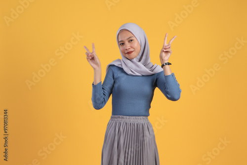 Canvas Print happy asian indonesian muslim woman giving victory sign finger on isolated yello