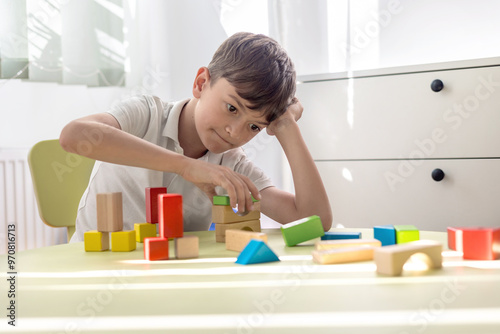 little boy playing with wooden blocks at children's table in bright room. The focus is on early child development and mental health, emphasizing the importance of speech therapy, psychological support