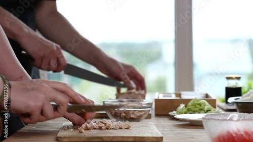 Daughter and mother cutting chicken fillet for sushi on the kitchen table