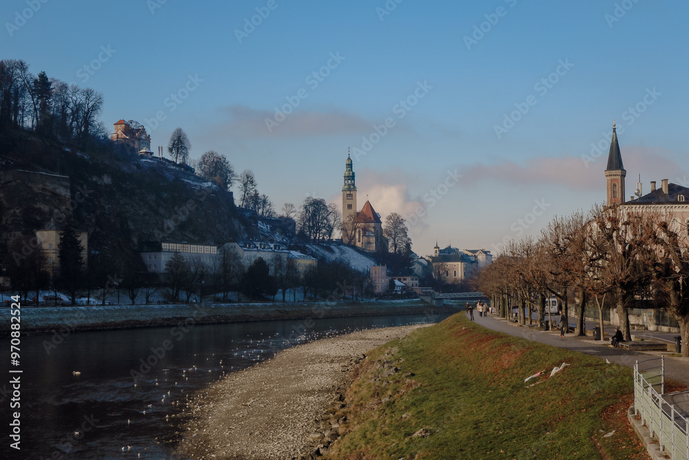 Obraz premium Winter landscape of Salzburg along the riverbanks with historic architecture and serene winter scenery at dusk