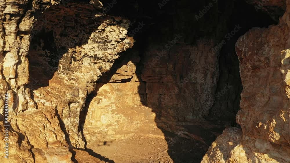 Sunlight illuminating the entrance of a mysterious cave hidden within a rugged rock formation. Drone flight entering the cave Sunlight illuminating the entrance of a mysterious cave hidden within a rugged rock formation. Drone flight entering the cave