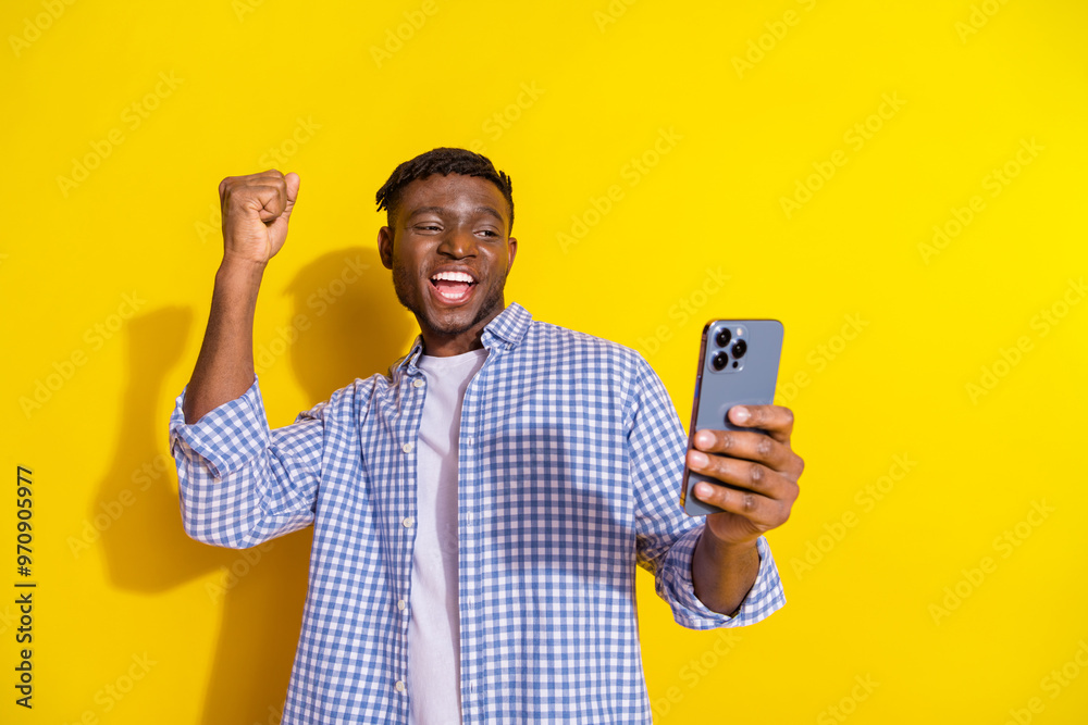 Photo of funky lucky guy dressed checkered shirt winning game modern device emtpy space isolated yellow color background Photo of funky lucky guy dressed checkered shirt winning game modern device emtpy space isolated yellow color background